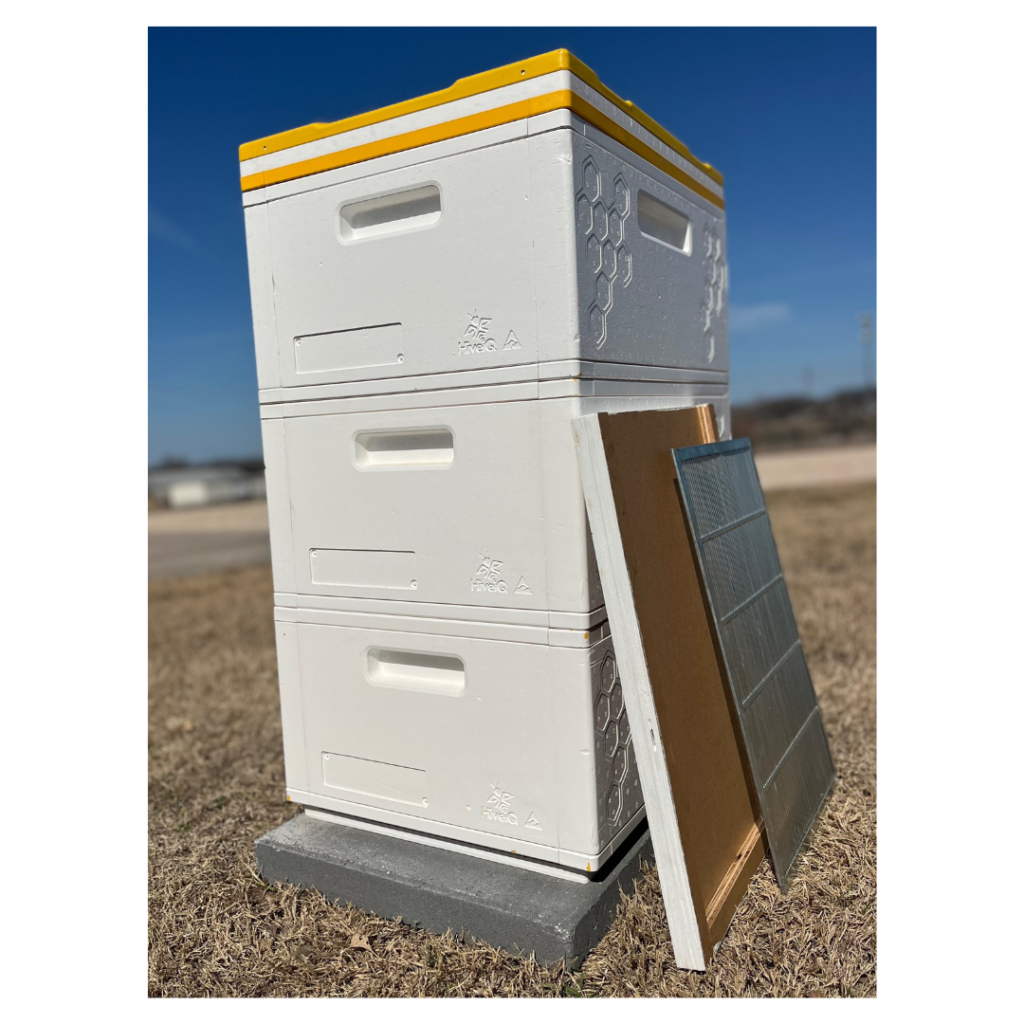 Stacked insulated beehive boxes with lid and frames leaning against the hive, used for housing and managing bee colonies outdoors.