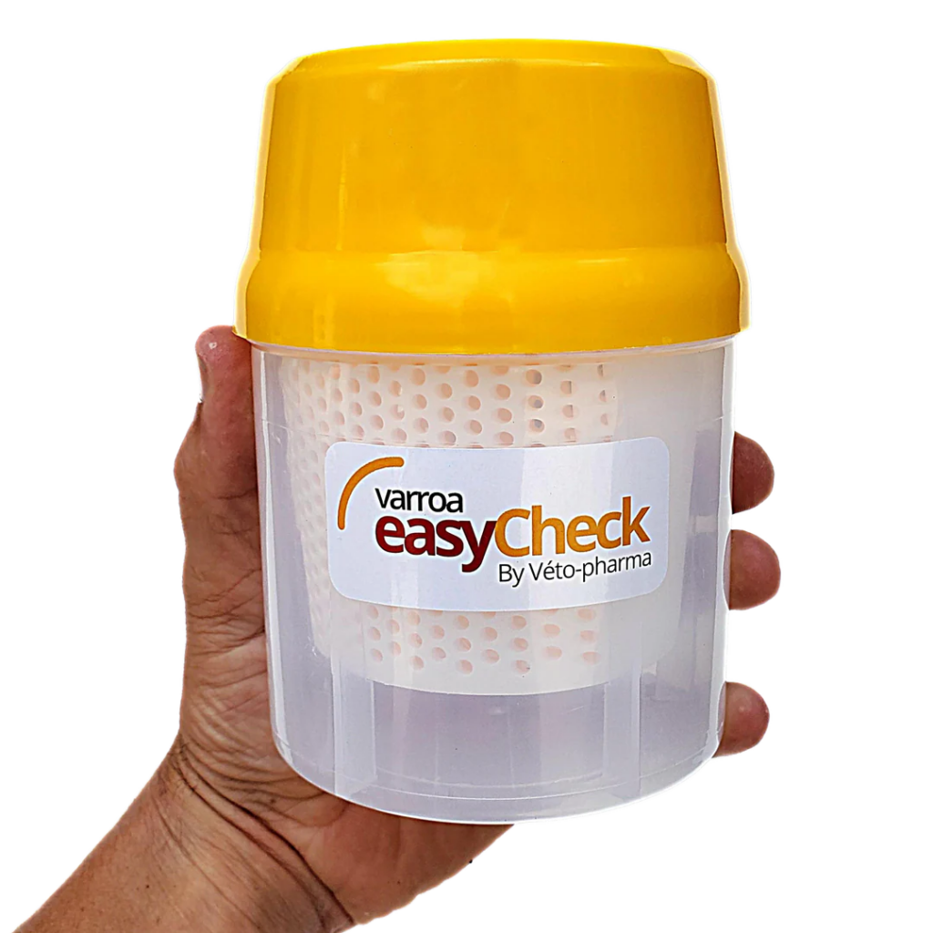 Hand holding a Varroa EasyCheck mite testing container with a yellow lid, used to monitor varroa mite levels in beehives.