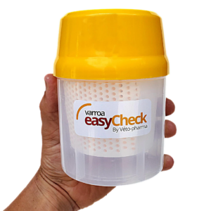 Hand holding a Varroa EasyCheck mite testing container with a yellow lid, used to monitor varroa mite levels in beehives.